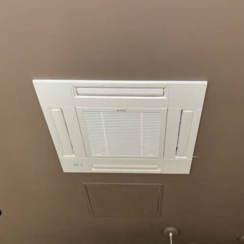 Climatiseur Cassette Mitsubishi : Installation au Plafond Climatiseur cassette Mitsubishi blanc encastré dans un plafond marron avec quatre volets de diffusion d'air.