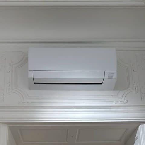 Climatiseur Mitsubishi : Installation Design et Discrète Climatiseur mural Mitsubishi Electric blanc installé au-dessus d'une porte avec des moulures décoratives élégantes.