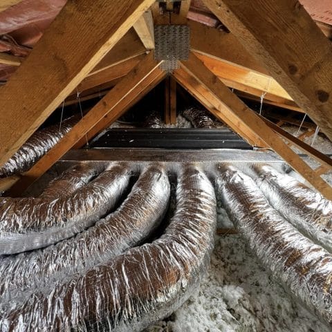 Ventilation et isolation des combles d'une maison Conduits de ventilation flexibles argentés et isolation de combles sous une charpente en bois de grenier.