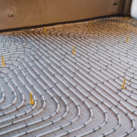 Installation de plancher chauffant : tubes et serpentins Installation de tubes blancs pour plancher chauffant disposés en serpentins sur un quadrillage au sol.