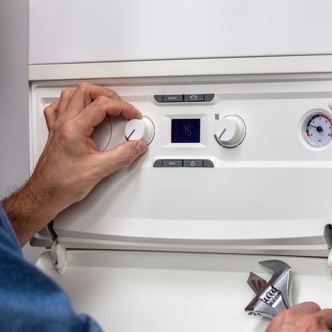 Réglage et entretien de chaudière : thermostat à 75°C Main ajustant le thermostat d'une chaudière affichant 75°C, manomètre et clé à molette à proximité.