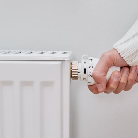 Régler son radiateur pour des économies d'énergie Main réglant le bouton d'un thermostat de radiateur blanc affichant les chiffres 1, 2, 3 et 4.