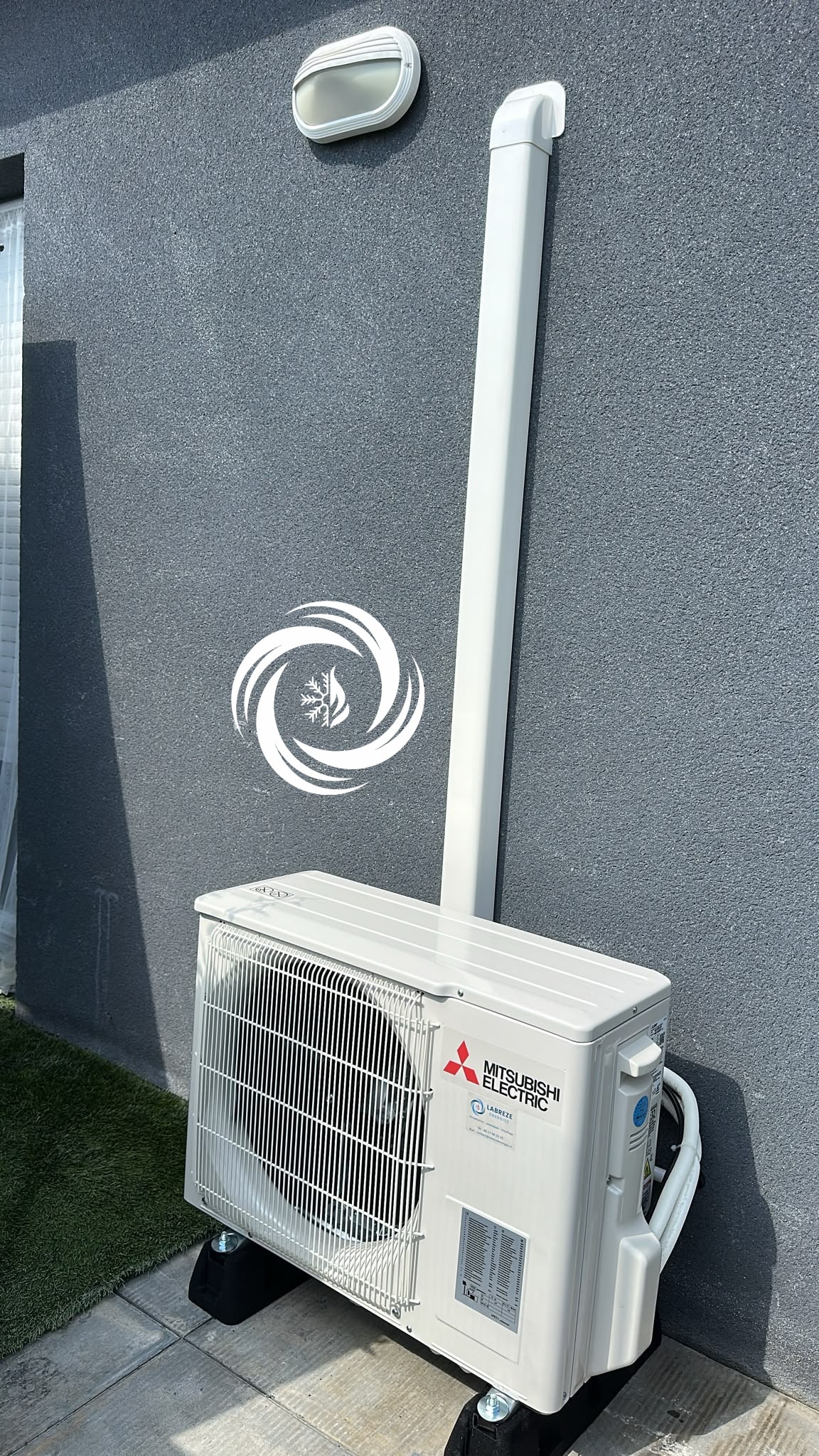 Installation Climatiseur Mitsubishi Electric Extérieur Unité Mitsubishi Electric installée sur mur gris avec conduit blanc et logo chauffage/climatisation.