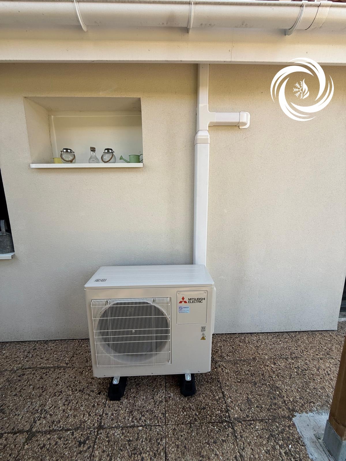 Installation Climatisation Mitsubishi Electric Extérieure Pessac Unité extérieure Mitsubishi Electric blanche sur terrasse gravillonnée avec goulotte murale.