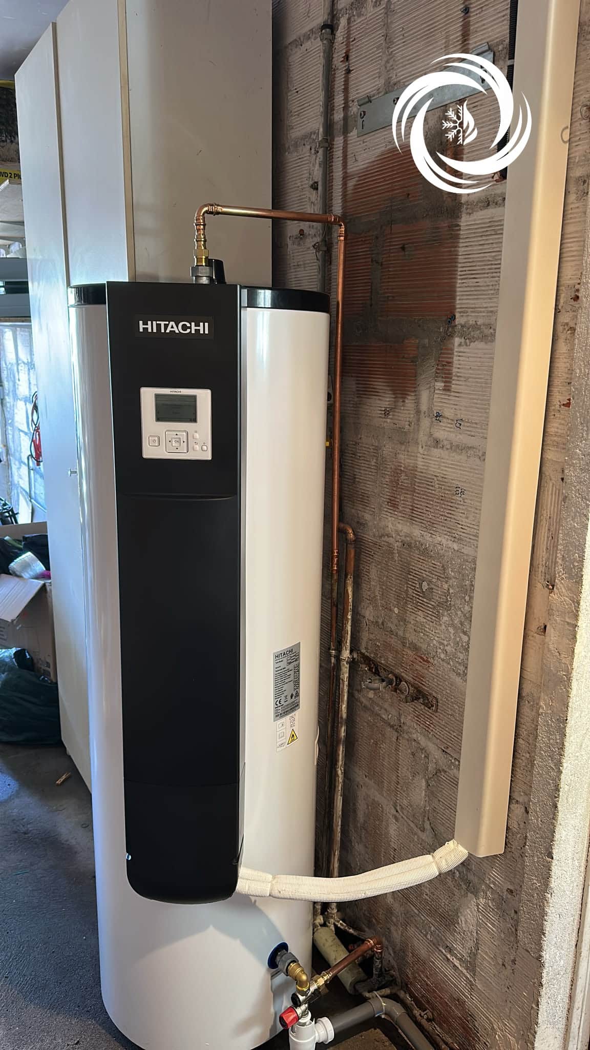 Installation chauffe-eau Hitachi Yutampo haute performance Chauffe-eau thermodynamique Hitachi Yutampo blanc et noir installé contre un mur en briques.