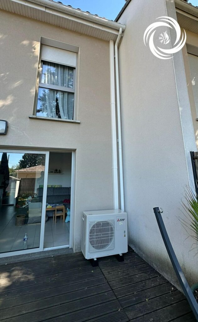 Unité Mitsubishi Electric sur terrasse bois, goulottes blanches sur façade beige.