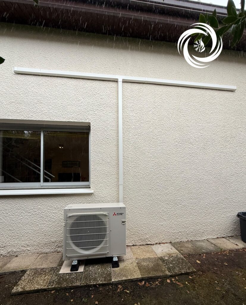 Unité extérieure de pompe à chaleur Mitsubishi Electric installée contre un mur crépi avec goulottes blanches.