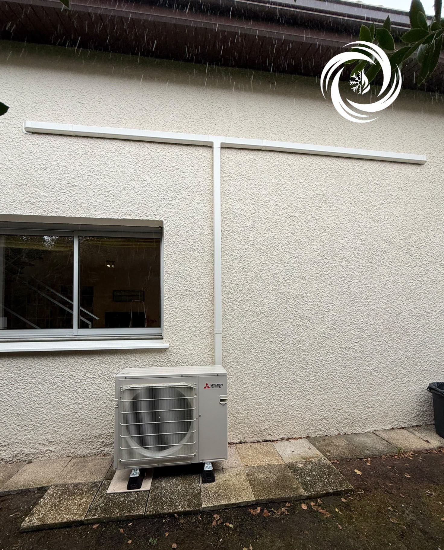 Pompe à Chaleur Mitsubishi Electric : Installation Extérieure Unité extérieure de pompe à chaleur Mitsubishi Electric installée contre un mur crépi avec goulottes blanches.